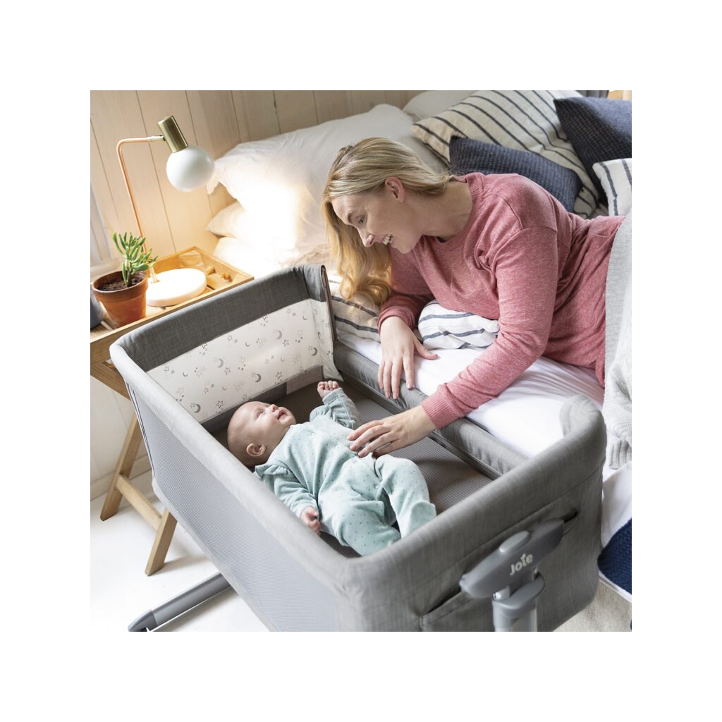 Mamička sa s láskou pozerá na spokojné bábätko v postieľke Joie Roomie Glide